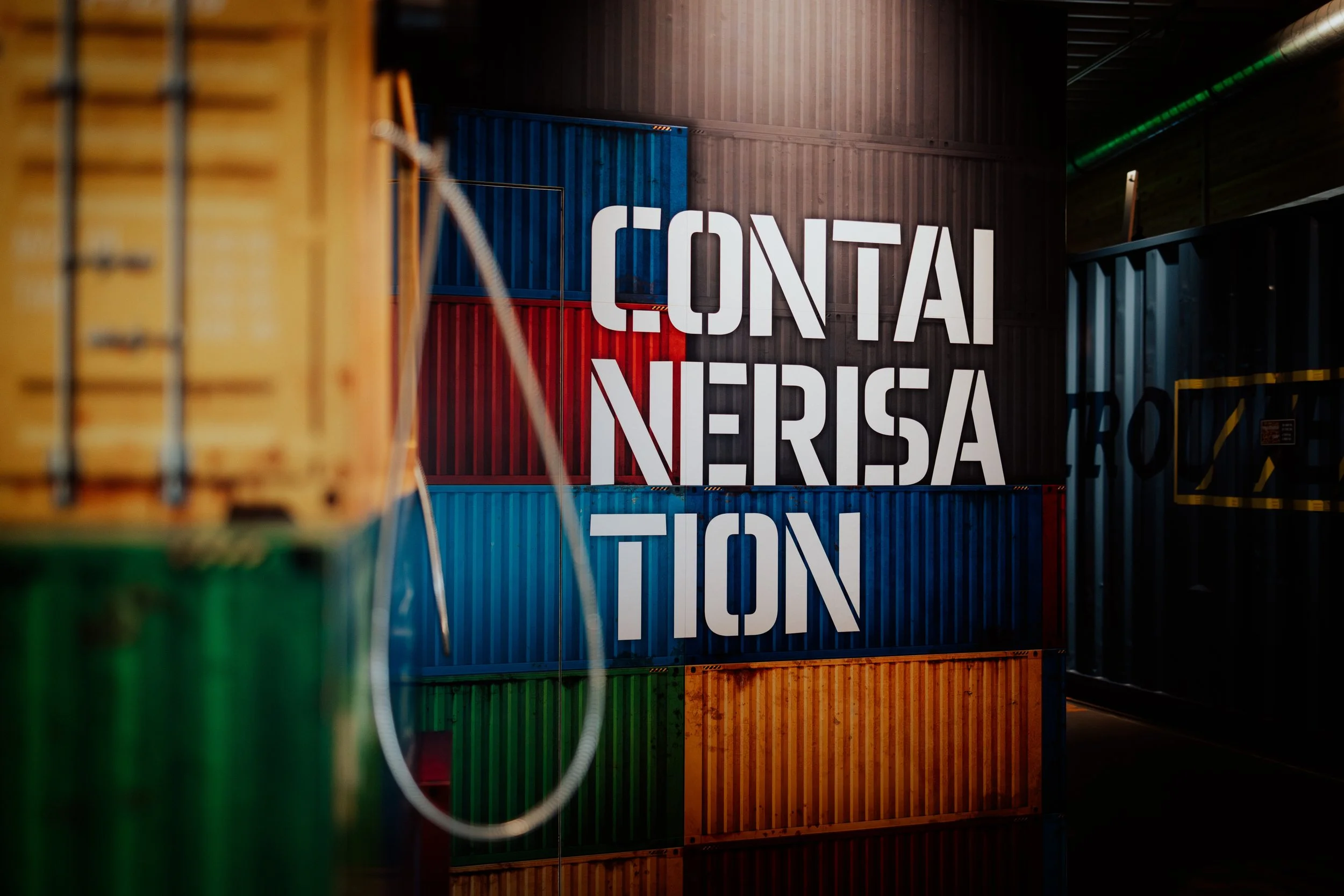 Mehrere bunte Container und das Wort "CONTAINER" an einer Wand in einem Lagerraum.