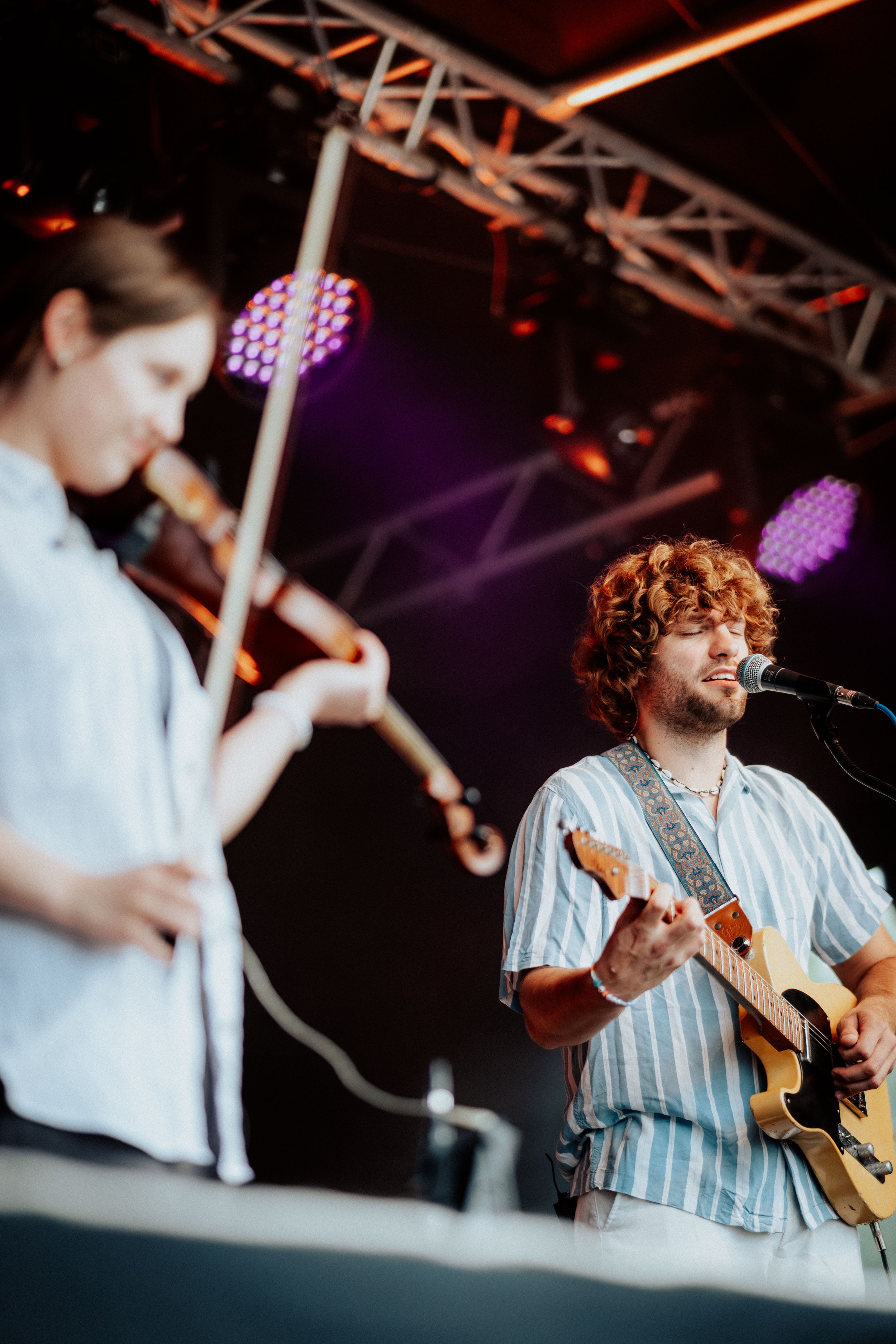 Zwei Musiker, eine Frau mit Geige und ein Mann mit Gitarre, spielen auf einer Bühne bei einem Konzert.
