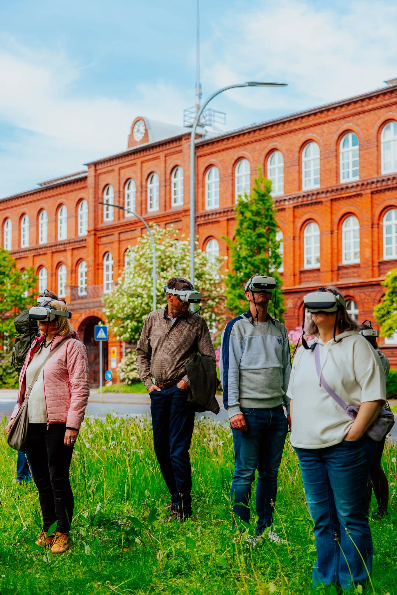 Menschen mit Virtual-Reality-Headsets in einem Park vor einem roten Backsteingebäude.
