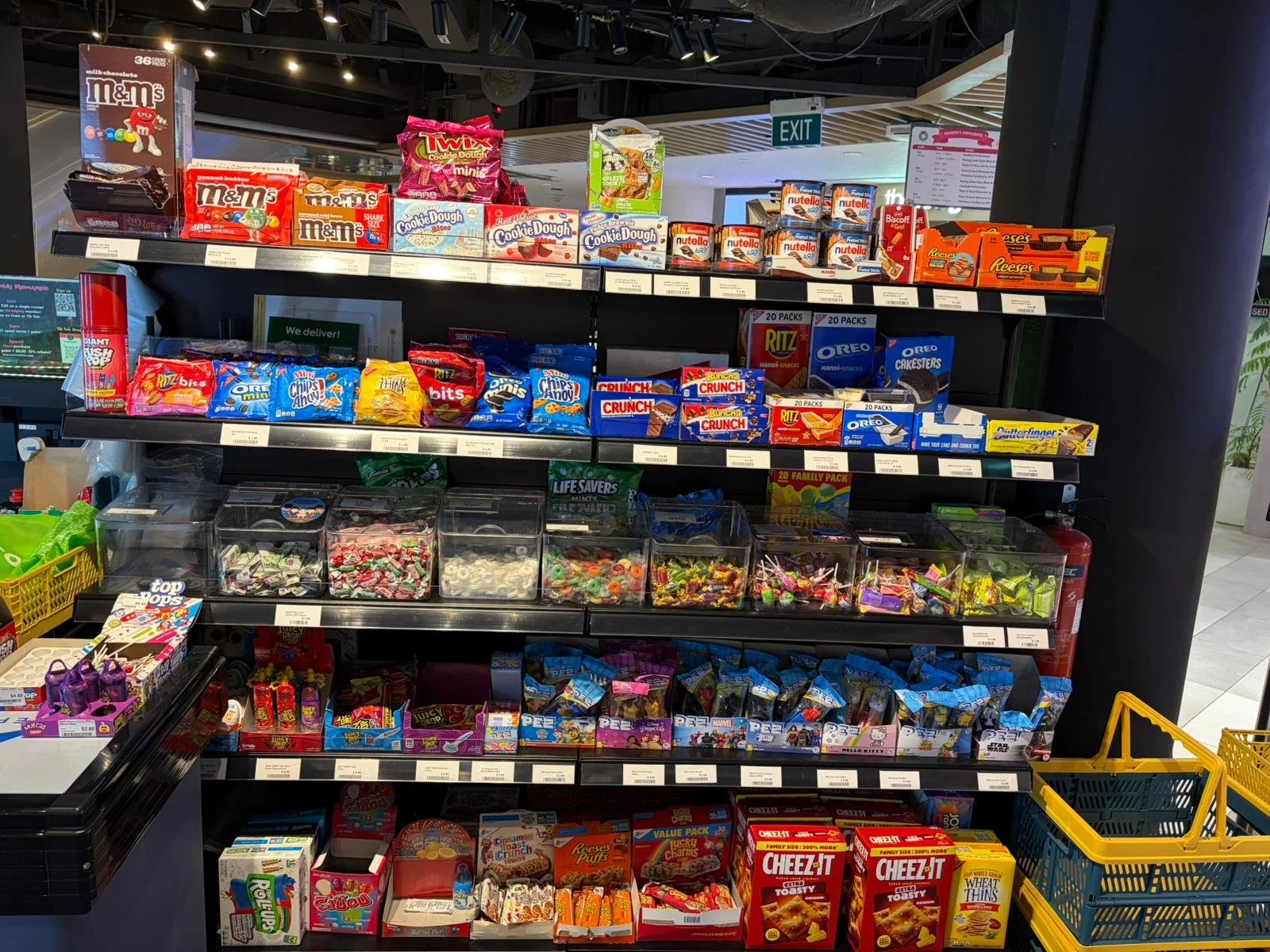 A store shelf stocked with various snack foods including candies, cookies, crackers, and chips.