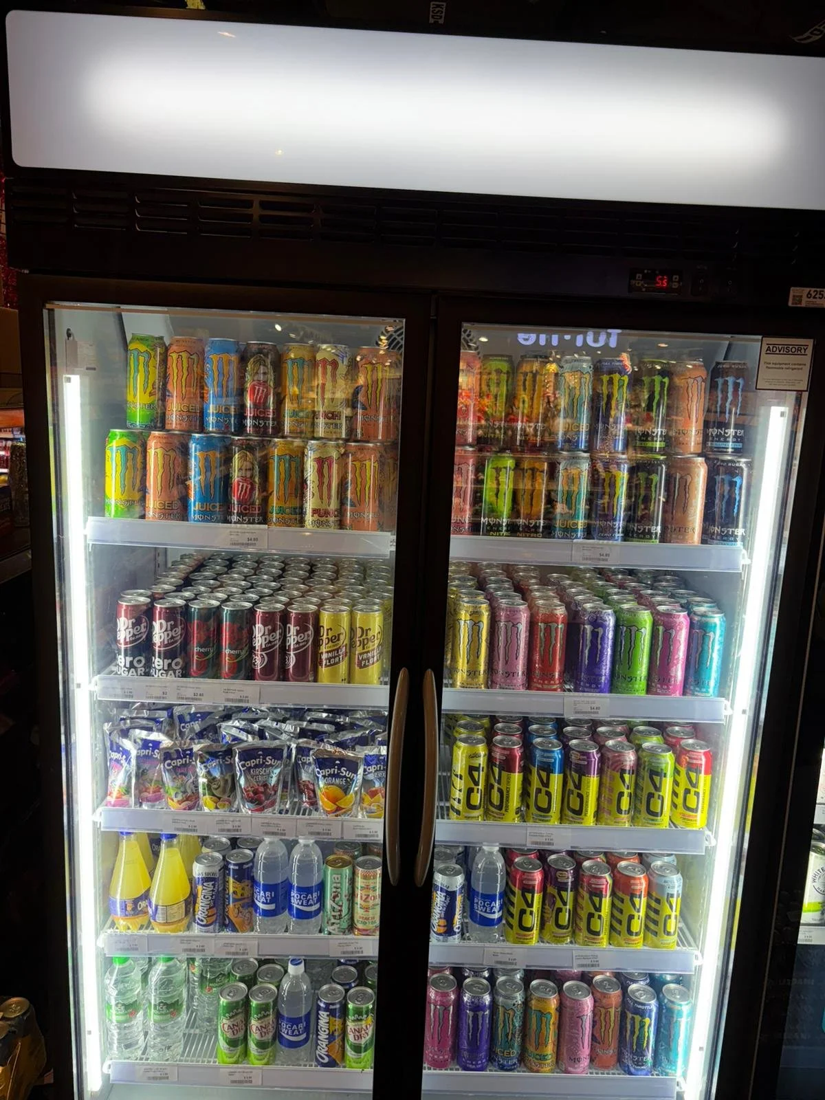 A refrigerated display case filled with various cans and bottles of beverages, including energy drinks, soda, and bottled water.