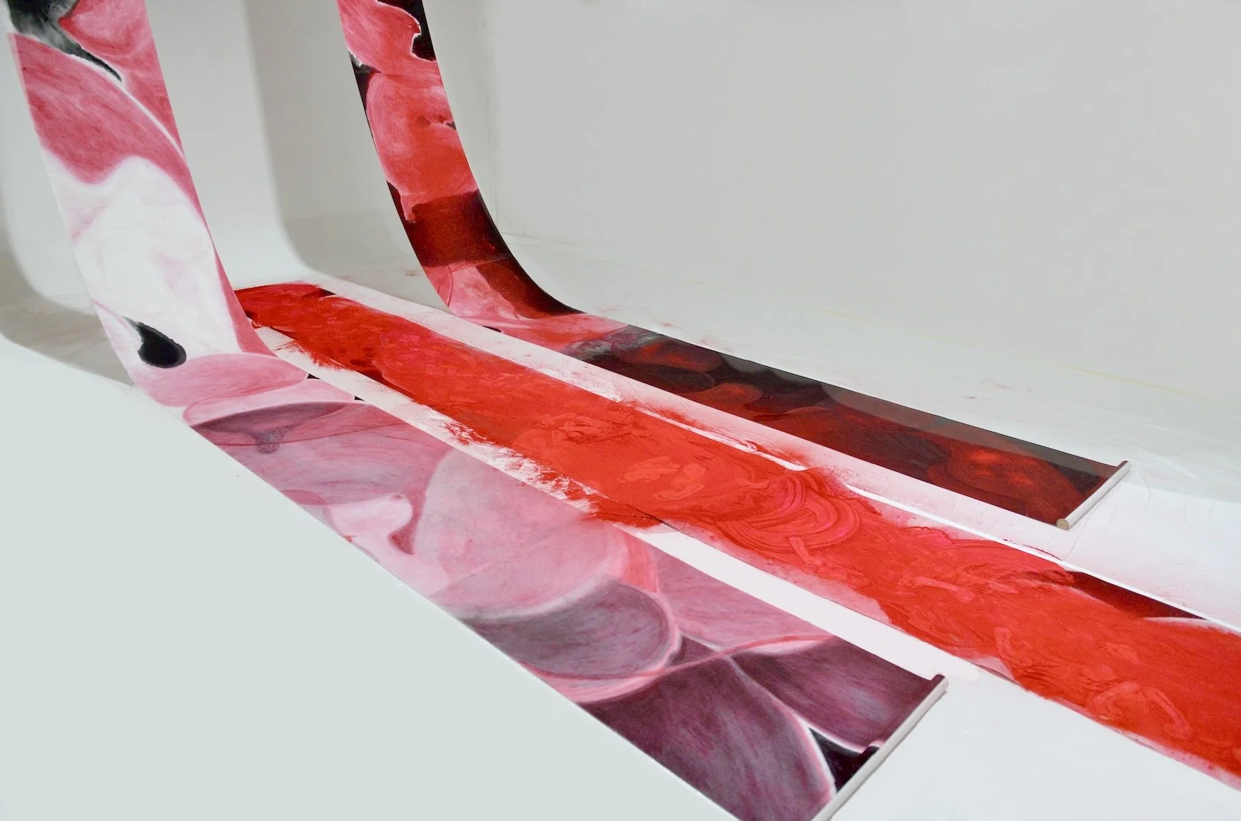 Decorative wrapping paper with pink, red, black, and white swirling abstract patterns, partially unrolled on a white surface.