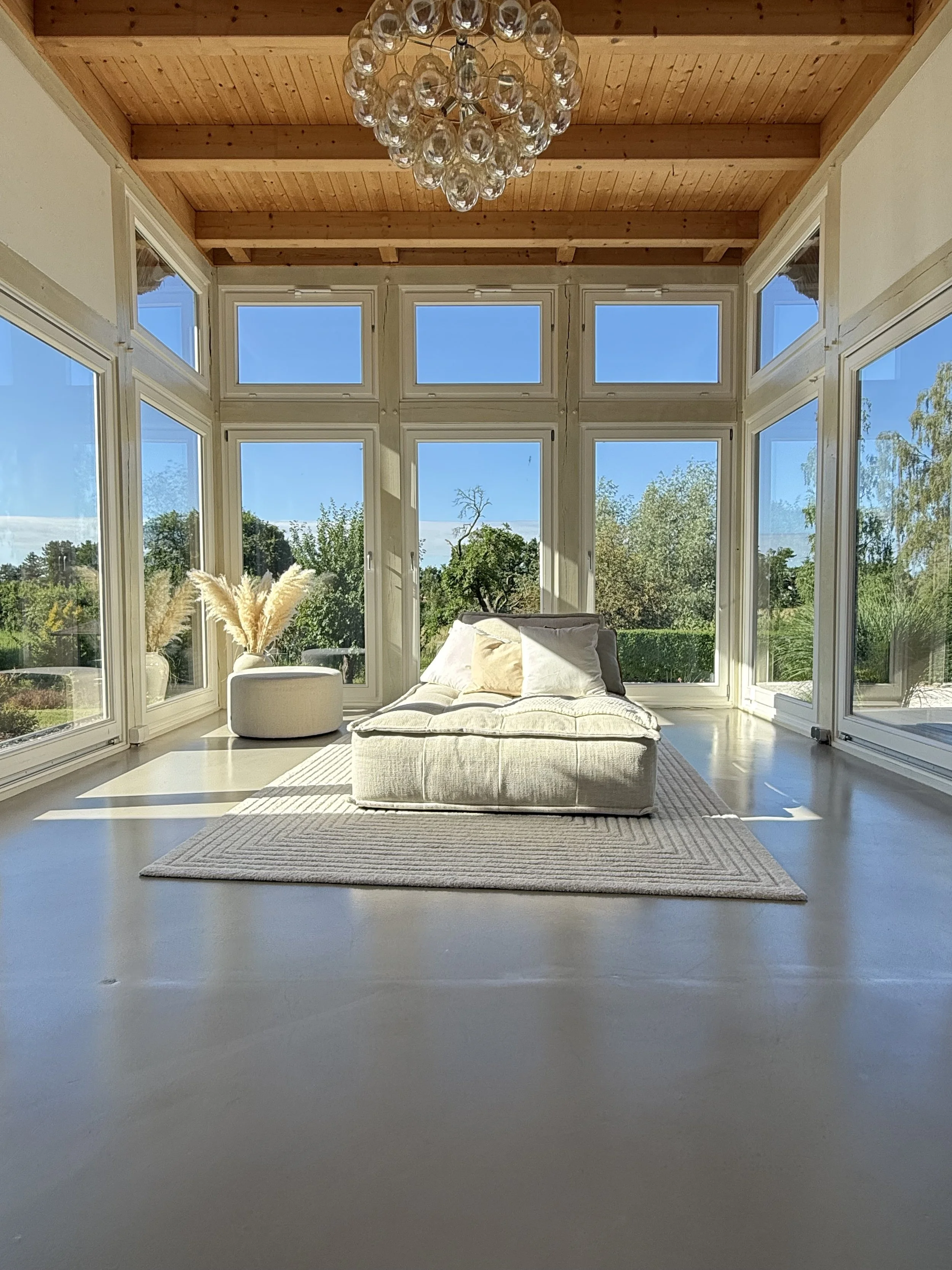 Helles Lounge-Setting im Wintergarten mit großen Fensterflächen und Gartenblick