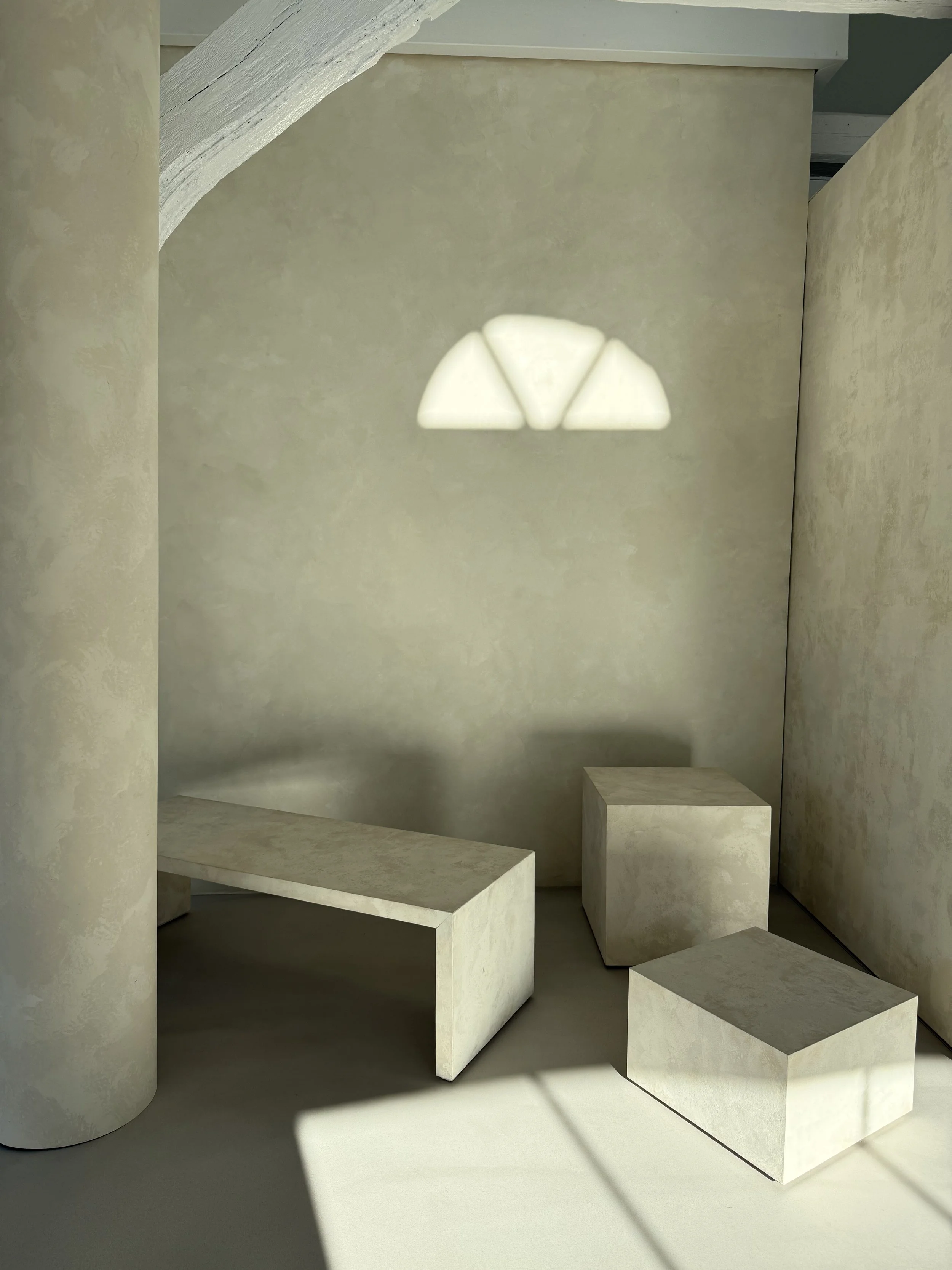 Minimalistisches Set mit strukturierter Wand, Podesten und grafischem Lichteinfall