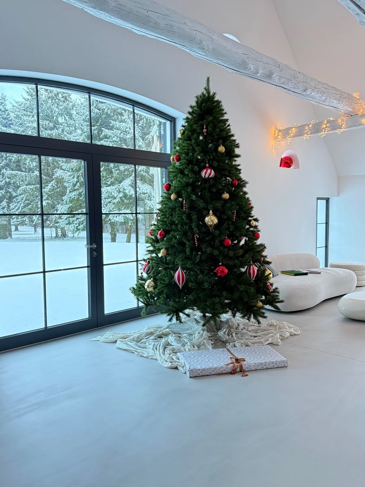 Weihnachtlich dekorierter Wohnbereich mit großem Weihnachtsbaum und Blick in den verschneiten Garten