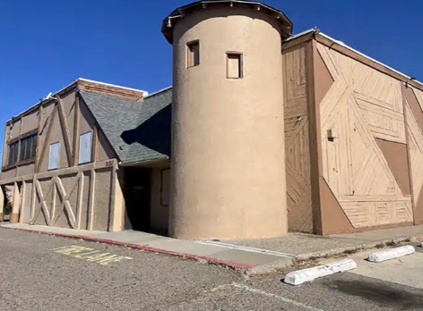 A building with a round tower and wooden barn-like walls under a clear blue sky.