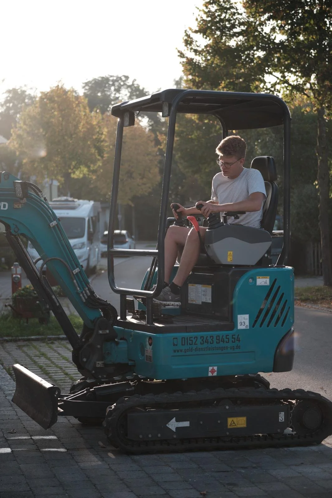 Junge sitzt in einer kleinen grünen Baggermaschine auf einer Straße bei Sonnenuntergang.