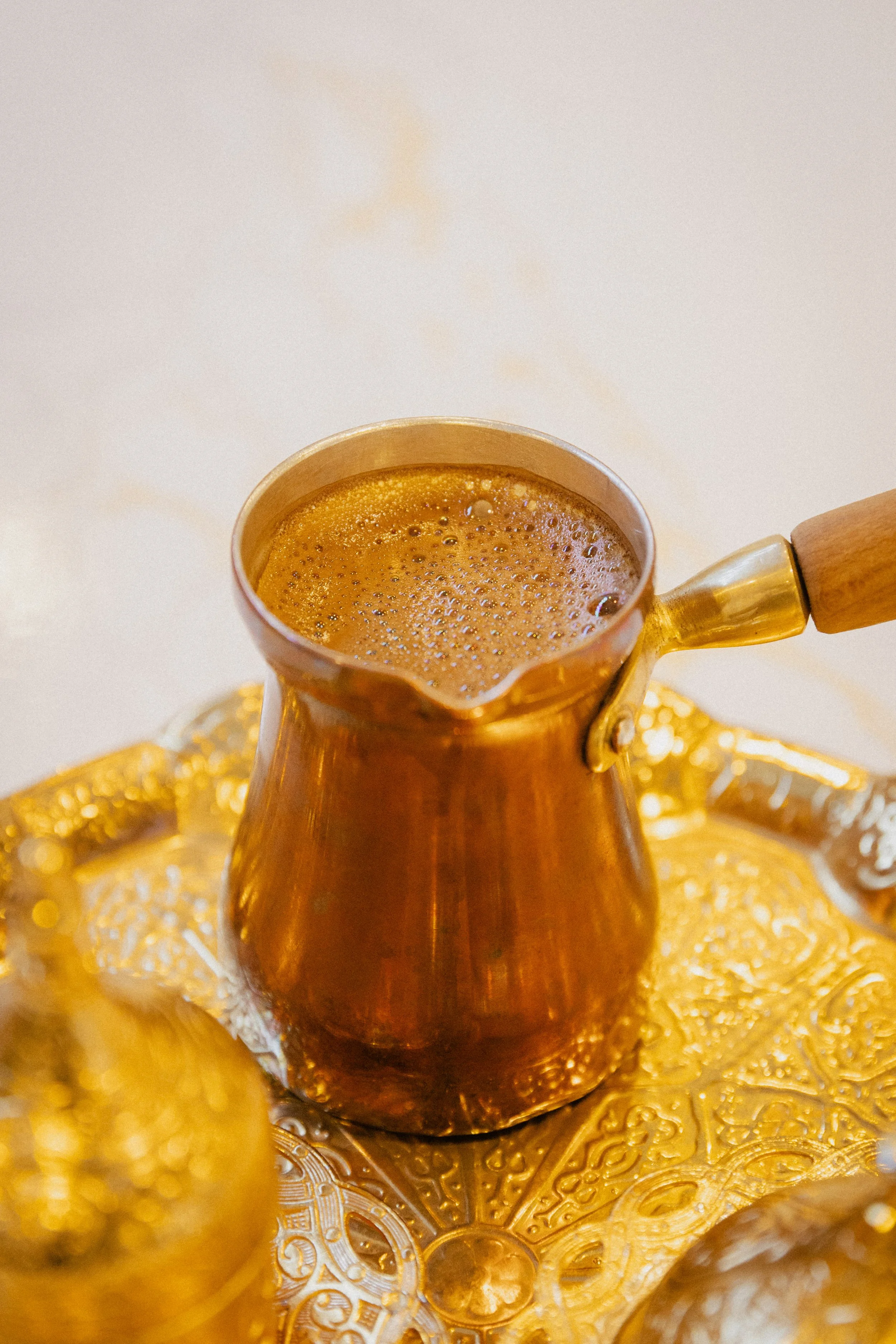 Copper coffee pot on a gold decorative tray with intricate patterns, filled with brewed coffee.