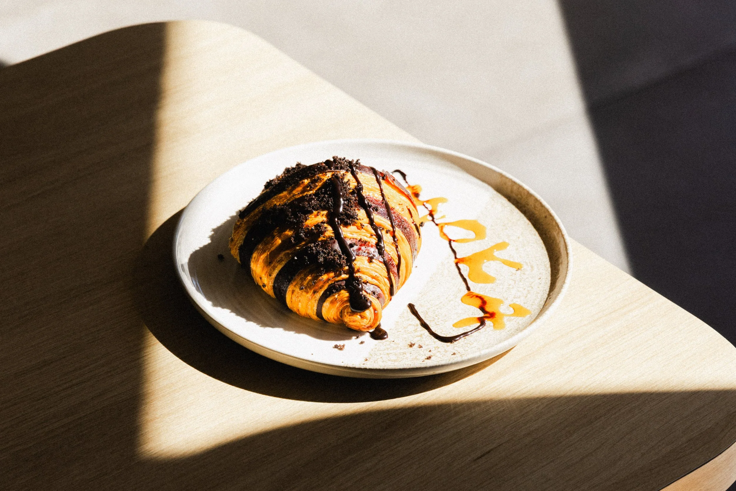 Chocolate and caramel drizzled croissant on a white plate with caramel and chocolate sauces