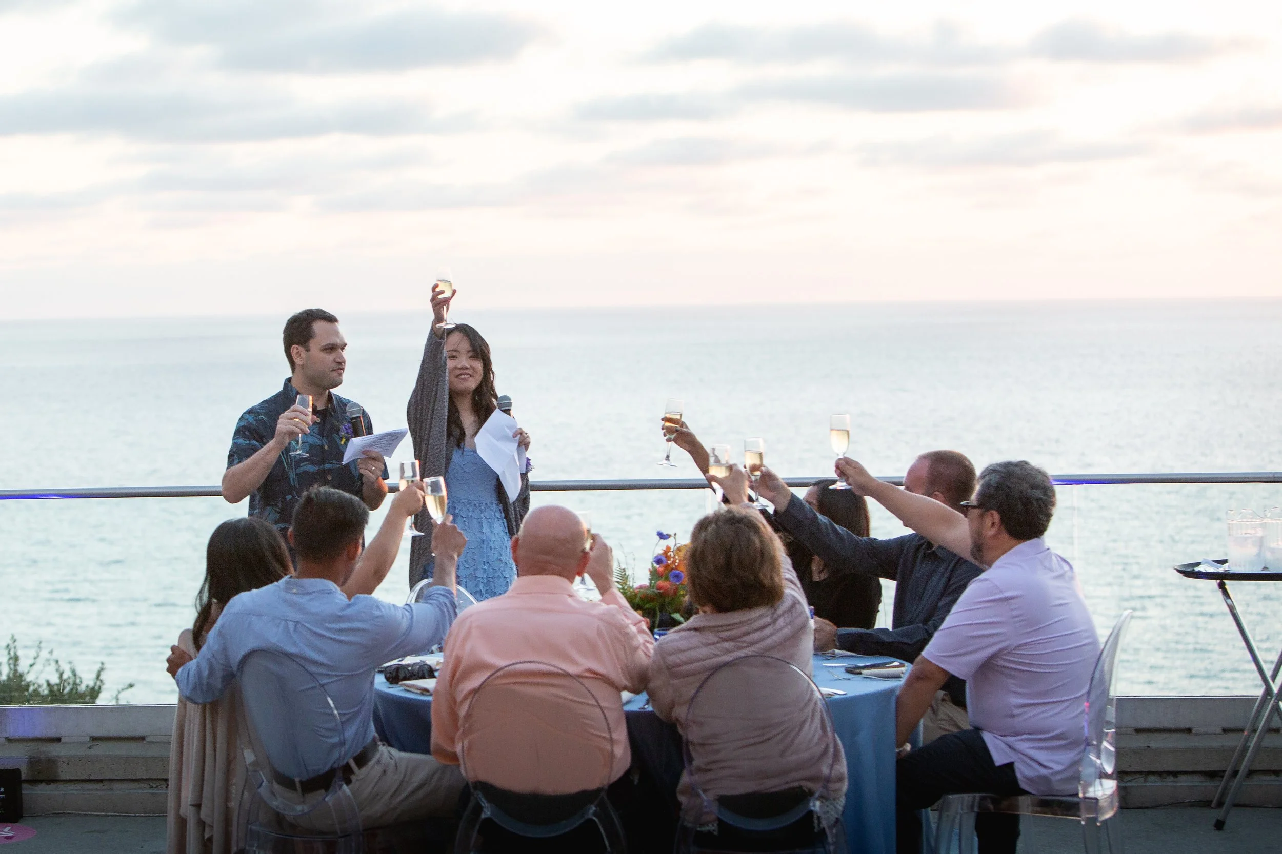 People celebrating with champagne on a boat deck overlooking the ocean, raising glasses for a toast at sunset.