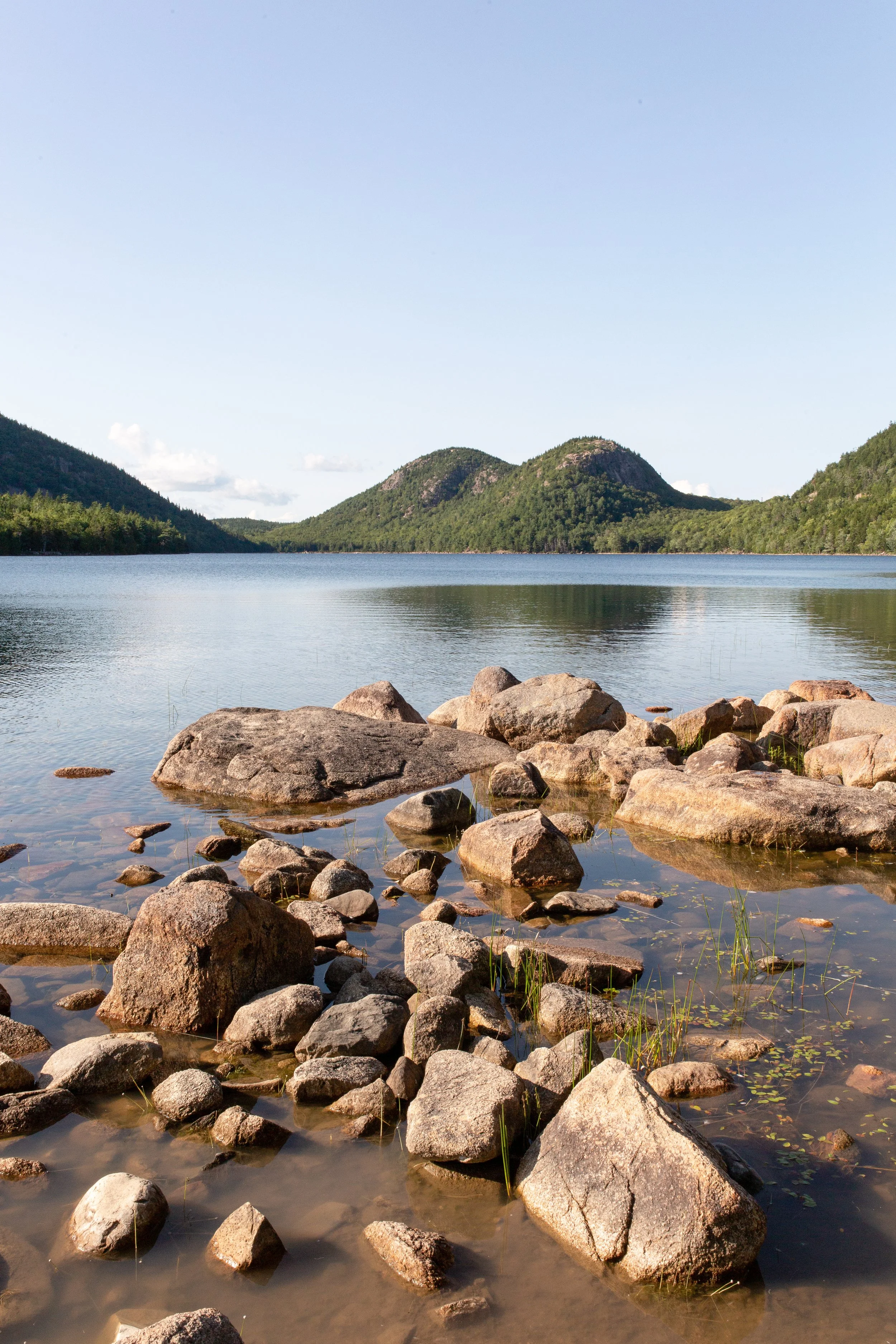 A rocky shoreline by a lake with mountains in the background under a clear sky.