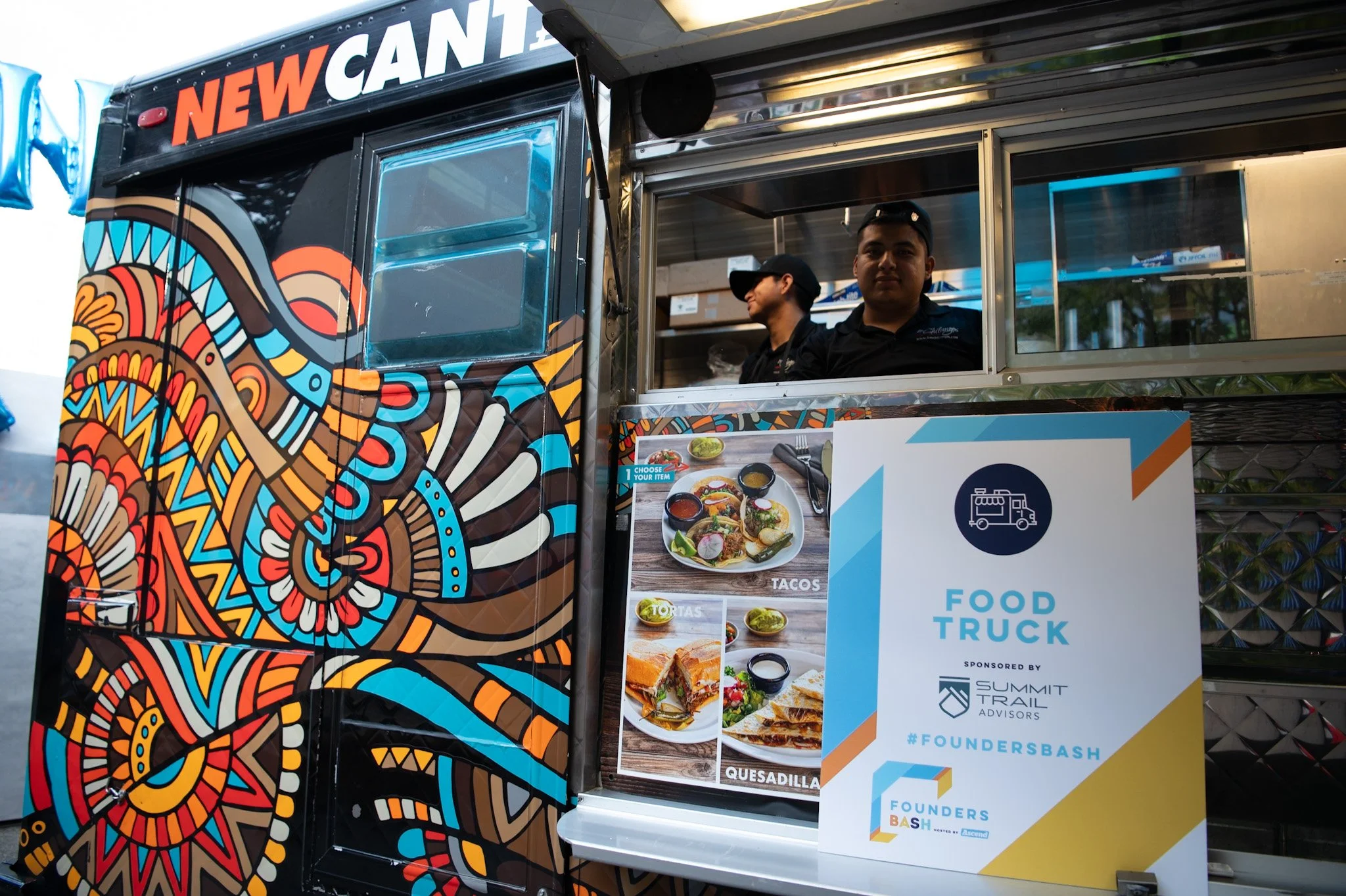 Colorful food truck with intricate geometric and abstract designs, serving tacos, quesadillas, and tortillas, with a sign indicating it is sponsored by Summit Trail Advisors for Founders Bash.