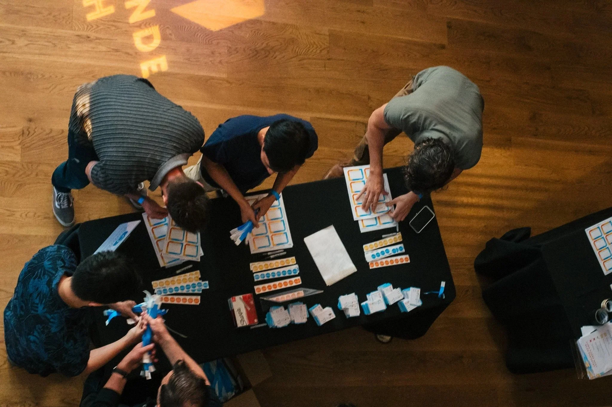 Four people working on a health-related educational activity at a table with chart cards, pamphlets, and a tablet, on a hardwood floor.