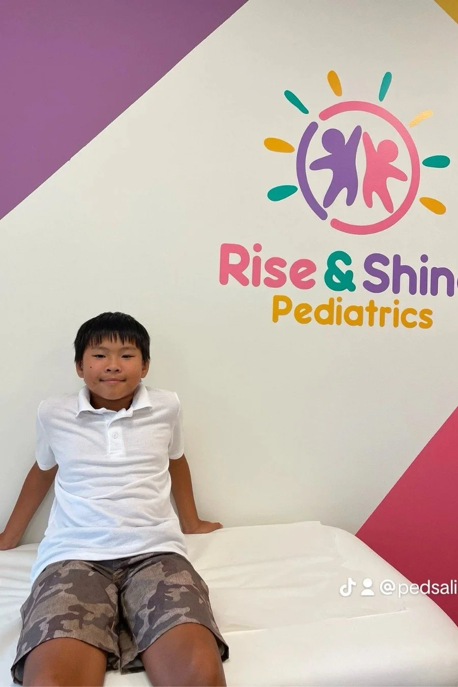 A child sitting on an exam table in front of the Rise & Shine Pediatrics logo