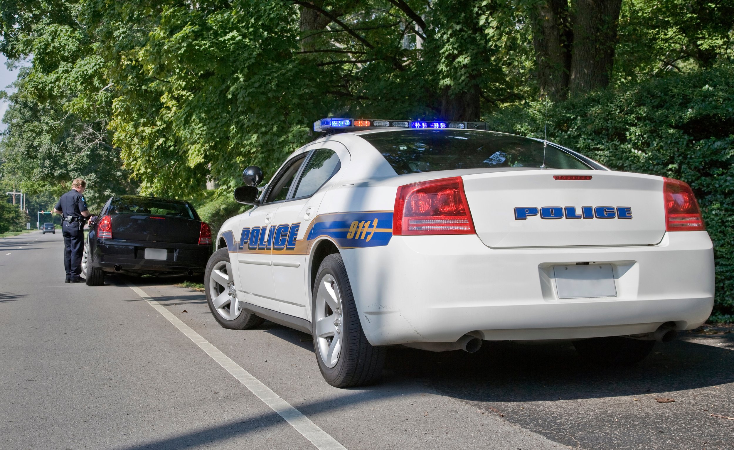 Police car and a black car on the shoulder with an officer near the drivers side in the background
