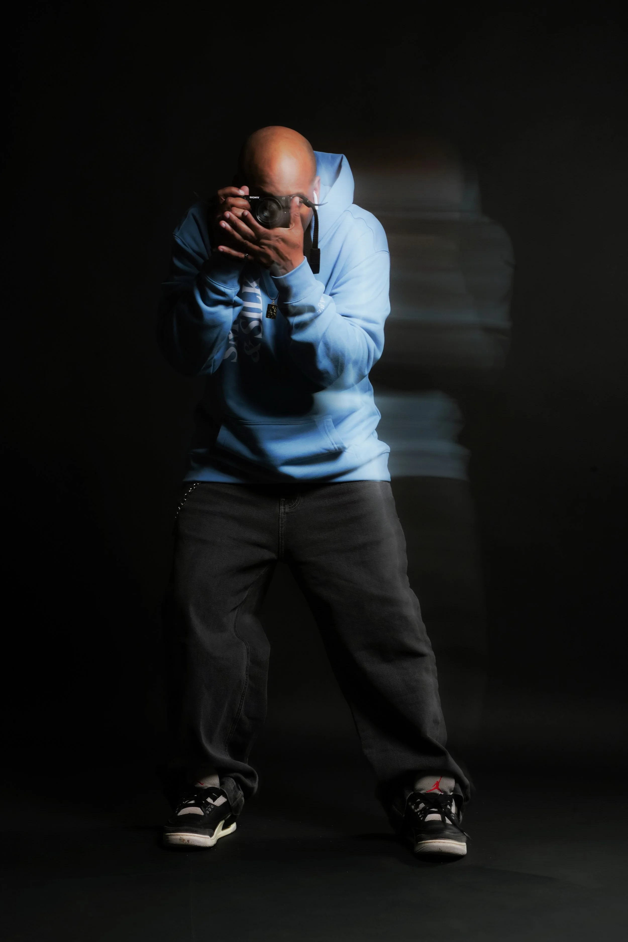 Person in blue hoodie taking a photo in a dark studio