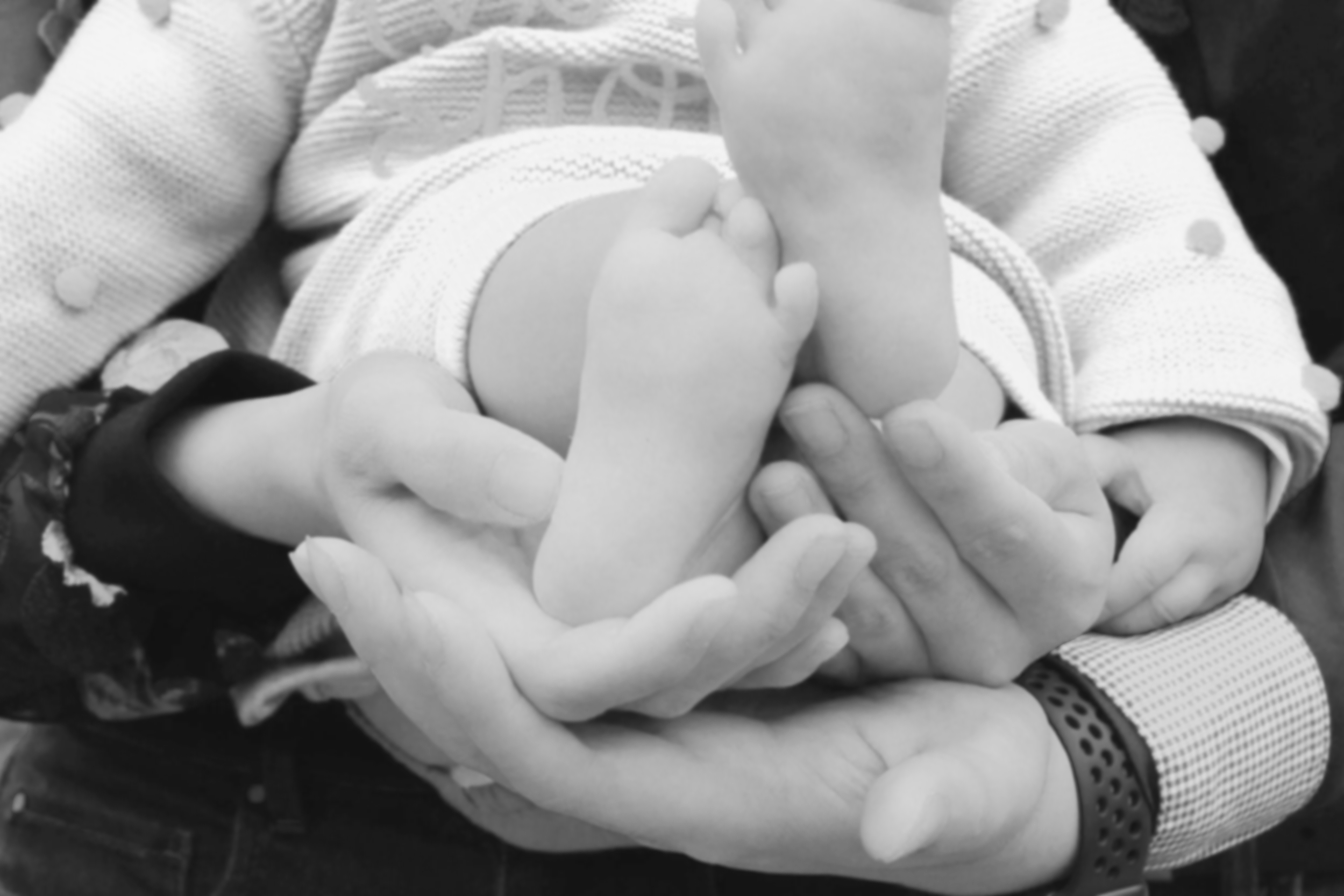 A person holding a small baby with both hands, supporting the baby’s feet and body.