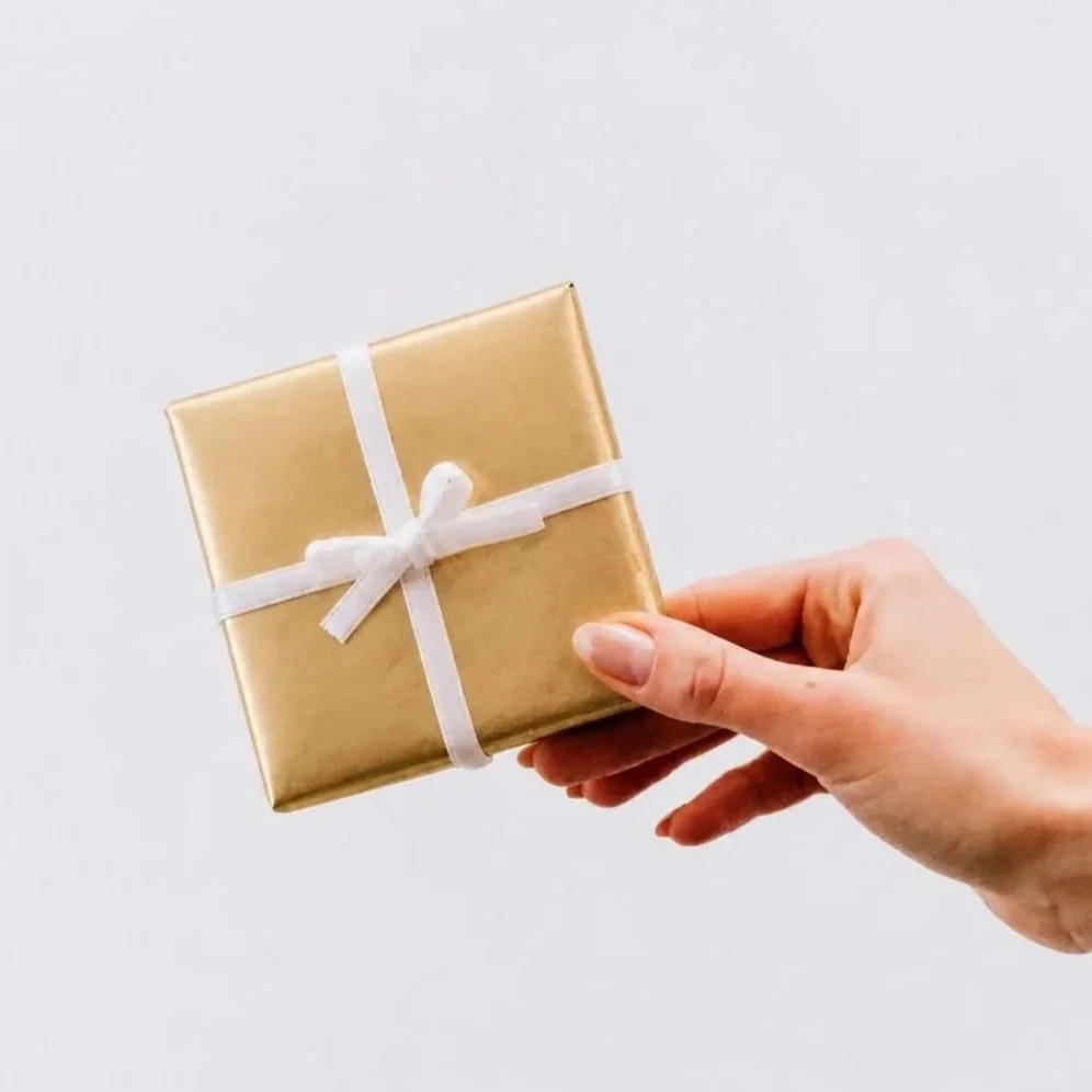 A hand holding a gift wrapped in gold paper with a white ribbon.