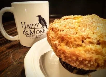 Coffee mug with bakery logo next to a large muffin on a plate