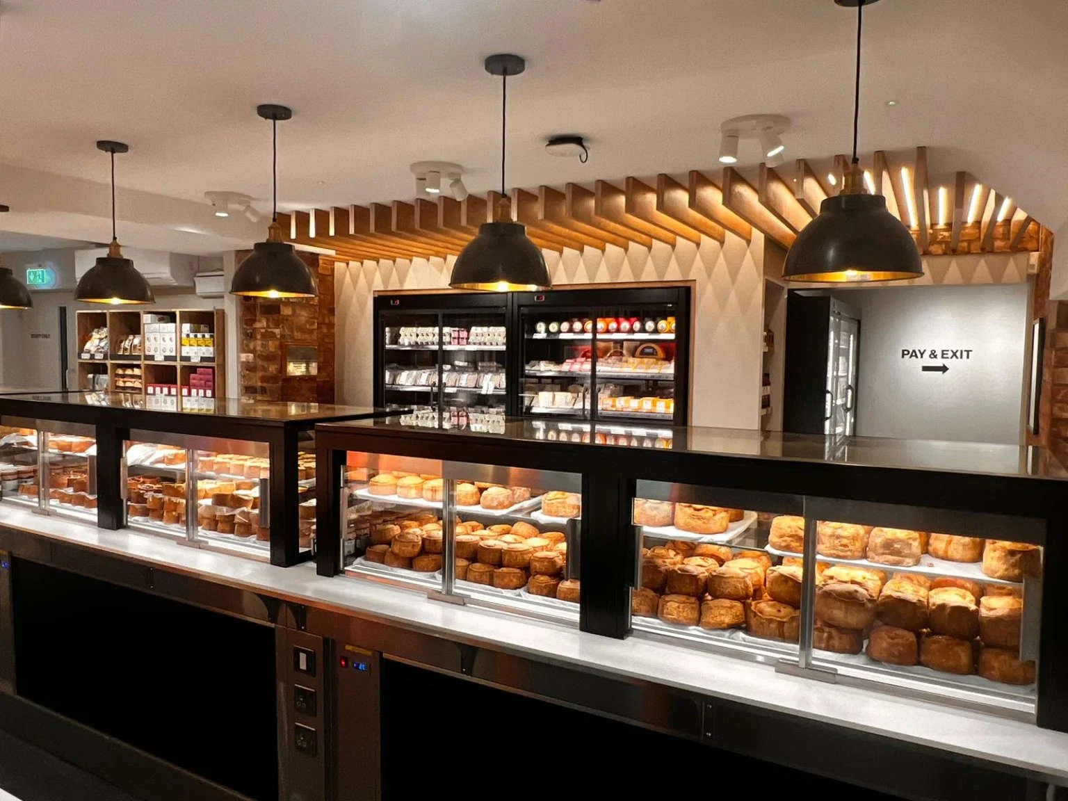 Display case filled with baked goods, including pastries and scones, in a bakery or cafe store with modern decor, pendant lights, and a sign indicating 'Pay & Exit'.