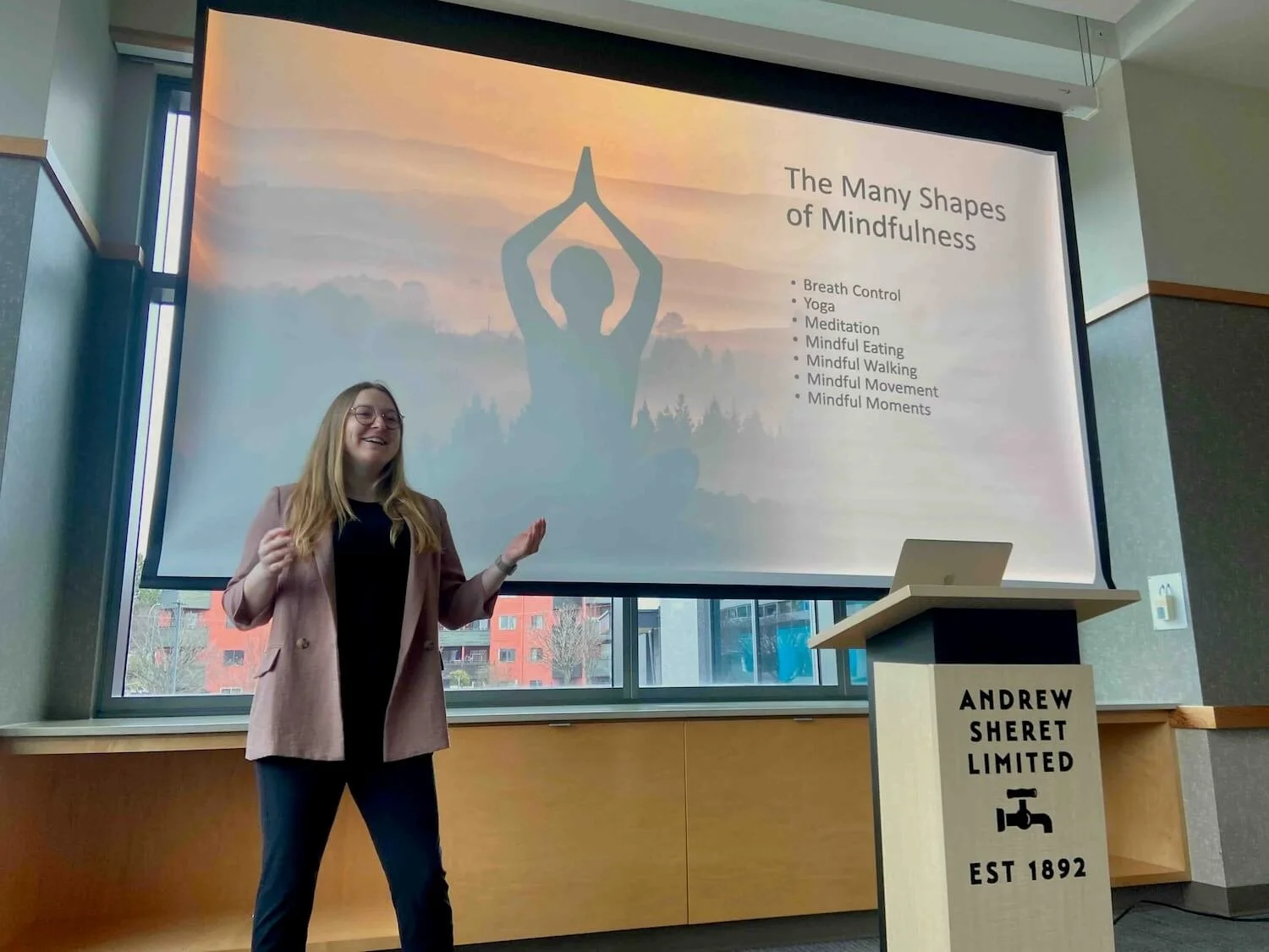 Cassi Starc OT pictured facilitating a lecture at podium with slideshow behind her.