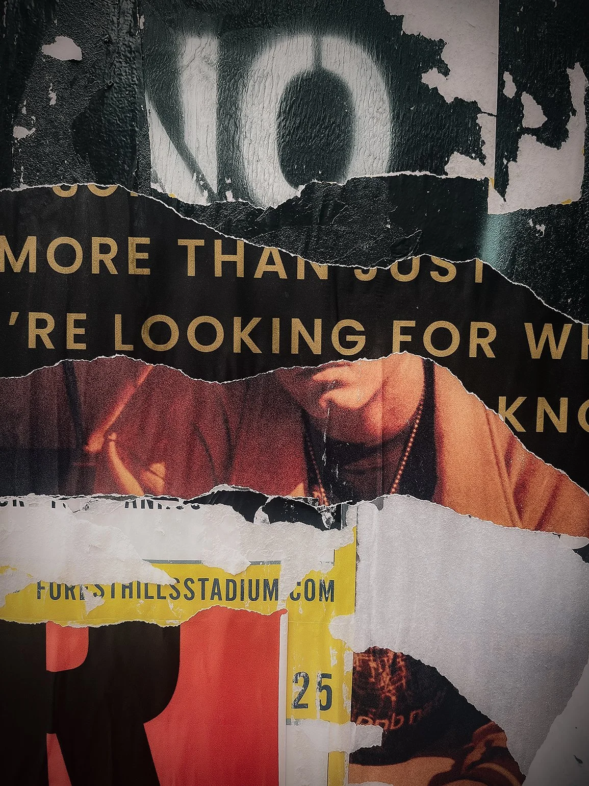 Torn poster featuring a black and white image of a person's face, a partly visible image of a person with necklaces, and a section of yellow text referencing a stadium website.