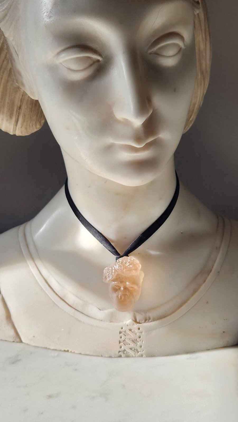 A light orange glass fancy gorilla pendant hanging around the neck of a marble model bust with velvet ribbon.