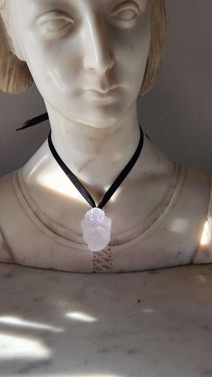A white glass fancy gorilla pendant hanging around the neck of a marble model bust with velvet ribbon.