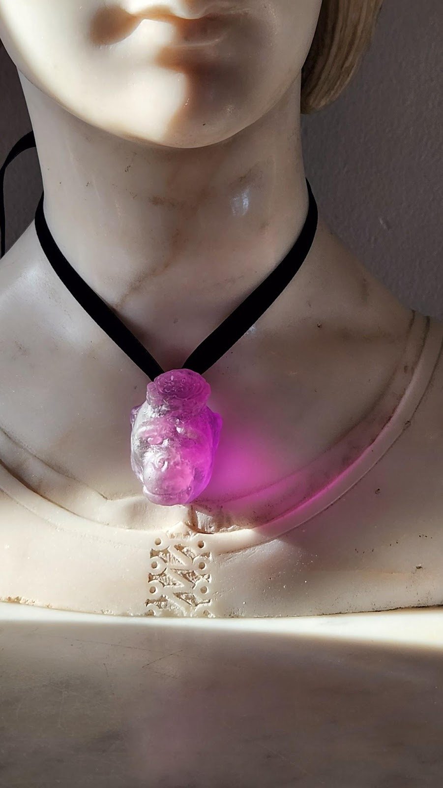 A purple glass fancy gorilla pendant hanging around the neck of a marble model bust with velvet ribbon.