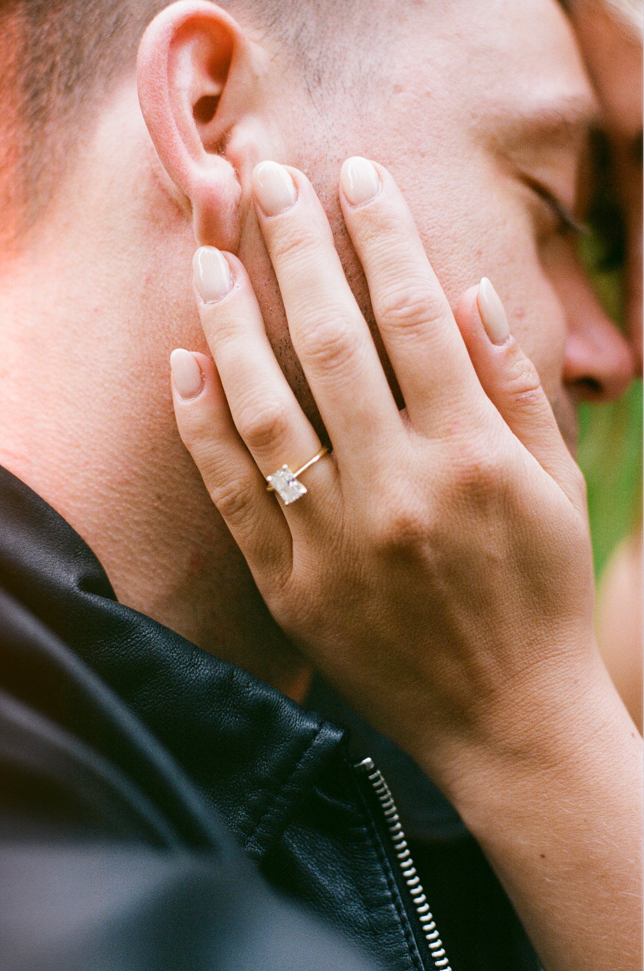 Close-up of a woman holding her hand with a ring on her ring finger, touching a man's face with an ear visible in the background.