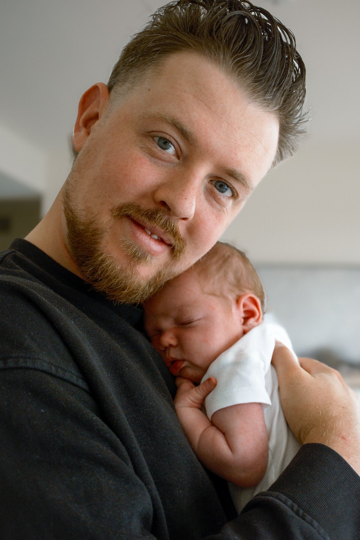 A man holding a sleeping baby close to his chest, wearing a black shirt.