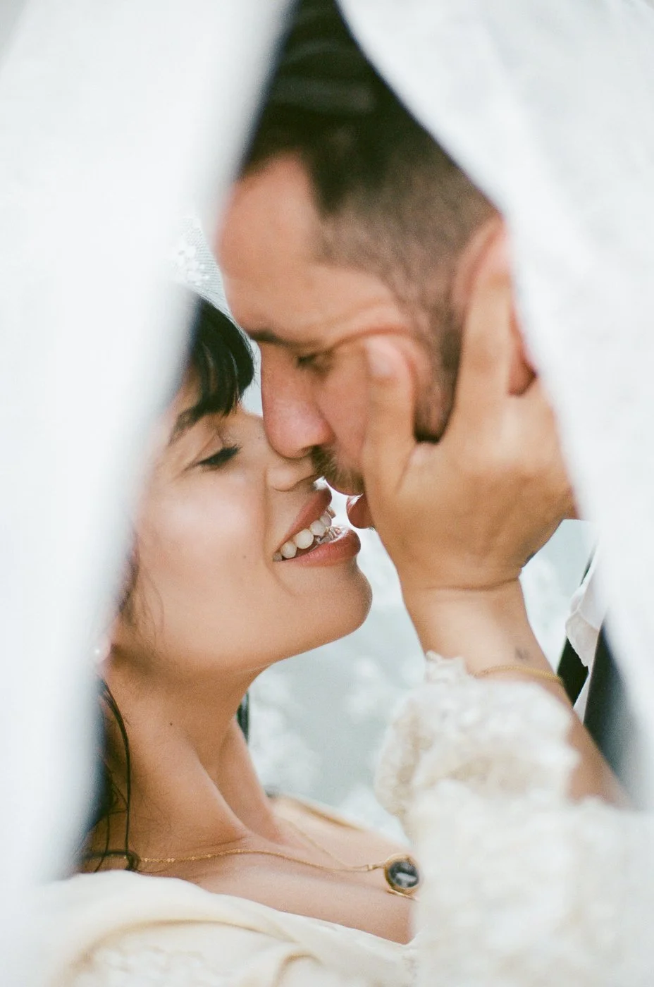 Couple in wedding attire holding hands outdoors with mountains in the background.