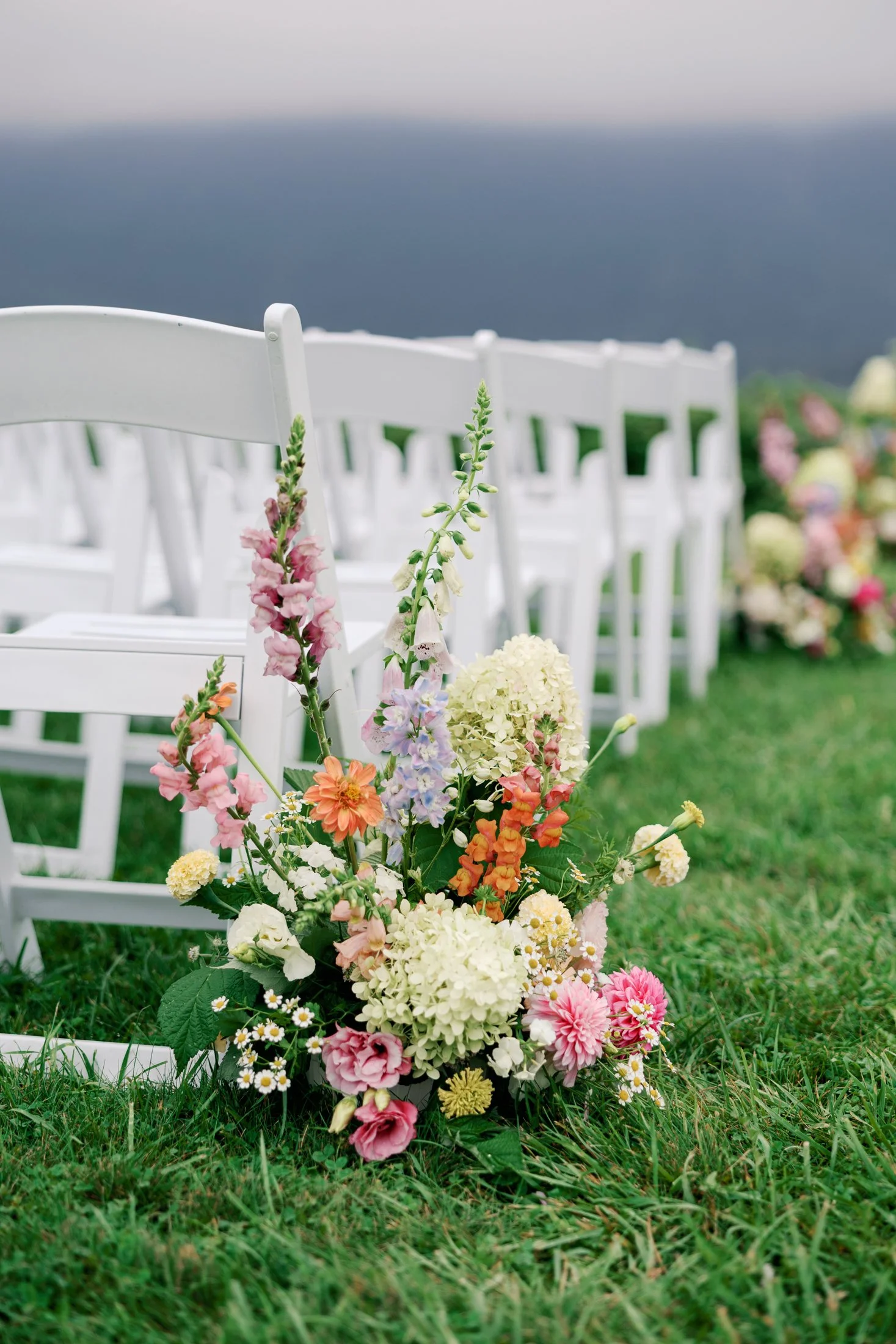 Fraser River Lodge ceremony site before guests arrive — elegant outdoor wedding ceremony chairs on grass with floral centre arrangement and sweeping mountain backdrop, captured in a hybrid film and digital wedding photography style.