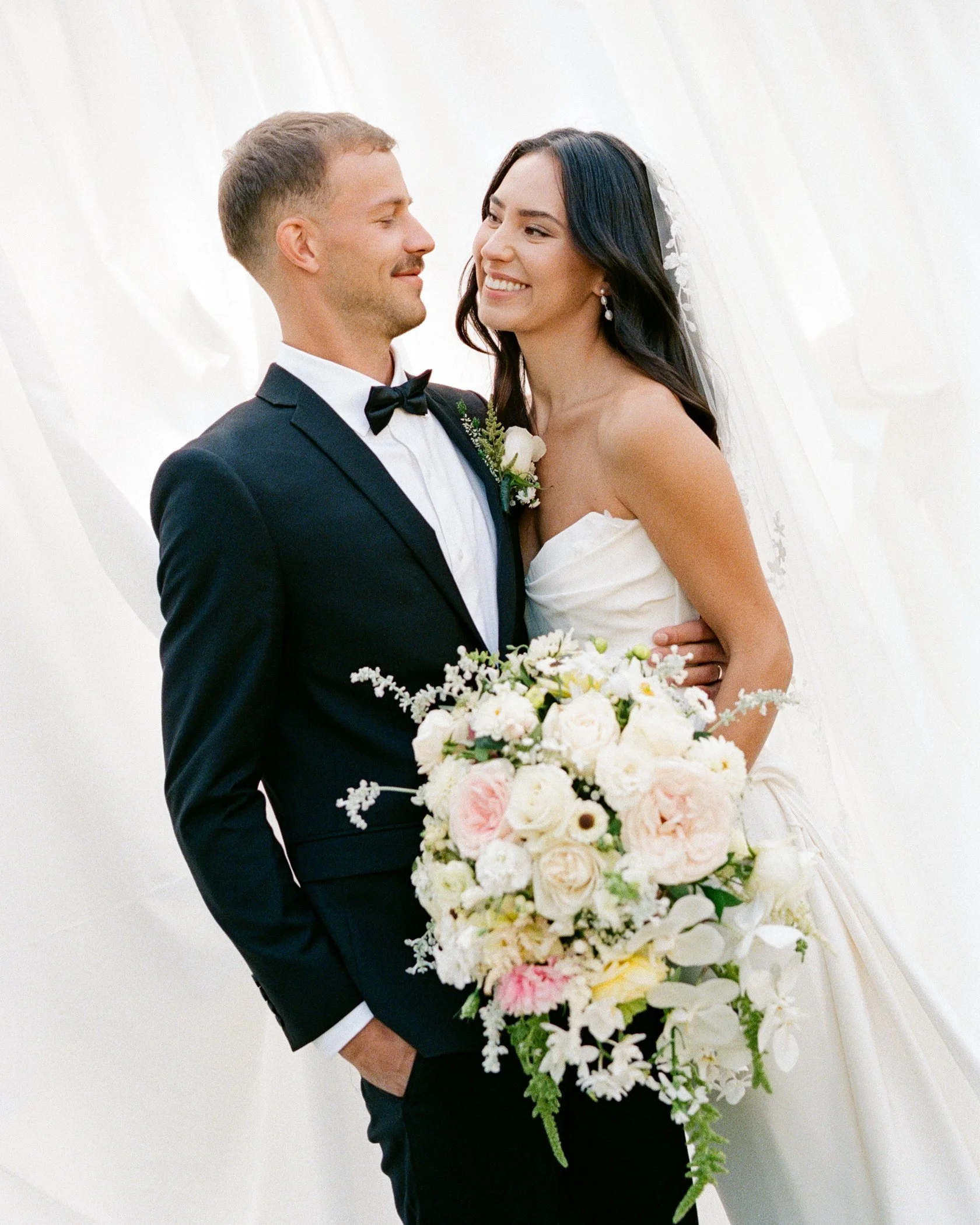 Couple in wedding attire holding hands outdoors with mountains in the background.
