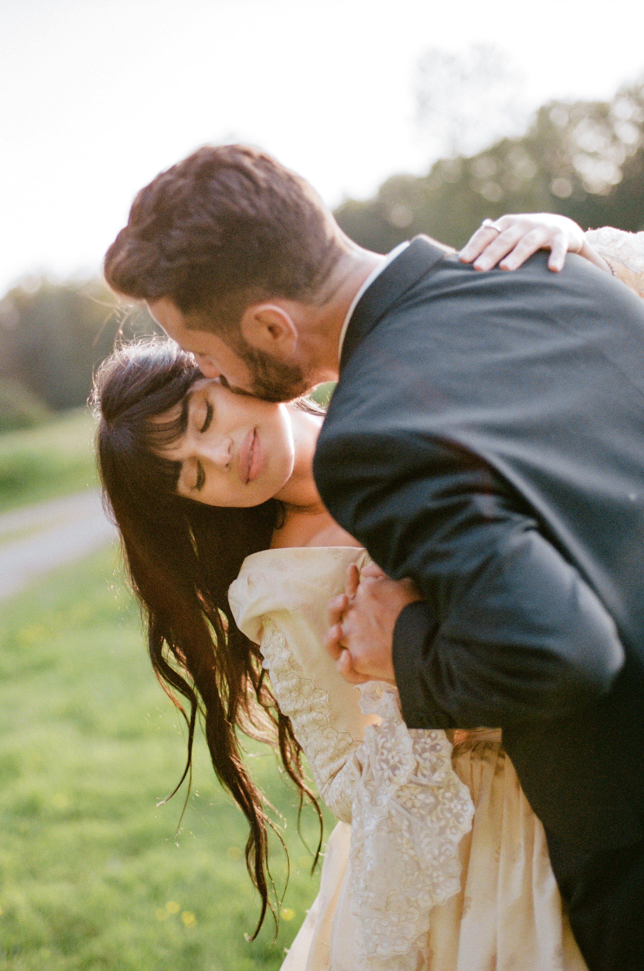 A bride and groom sharing a romantic dance outdoors during sunset, with the groom dipping the bride.