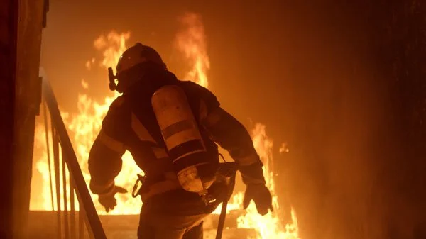 A firefighter bravely walks upstairs into a burning house