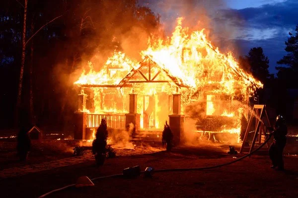 A house stands ablaze while firefighters fight to put it out