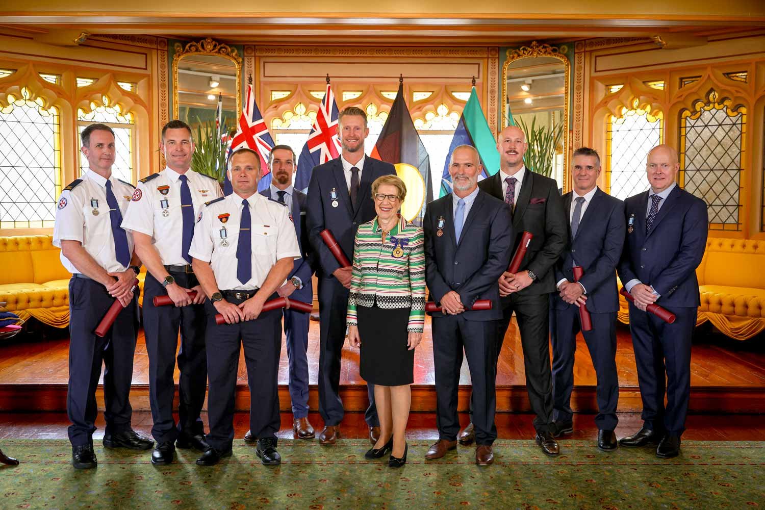 Proud Paramedic and rescue teams stand with Her Excellency the Governor, all are smiling as they proudly wear their medals.