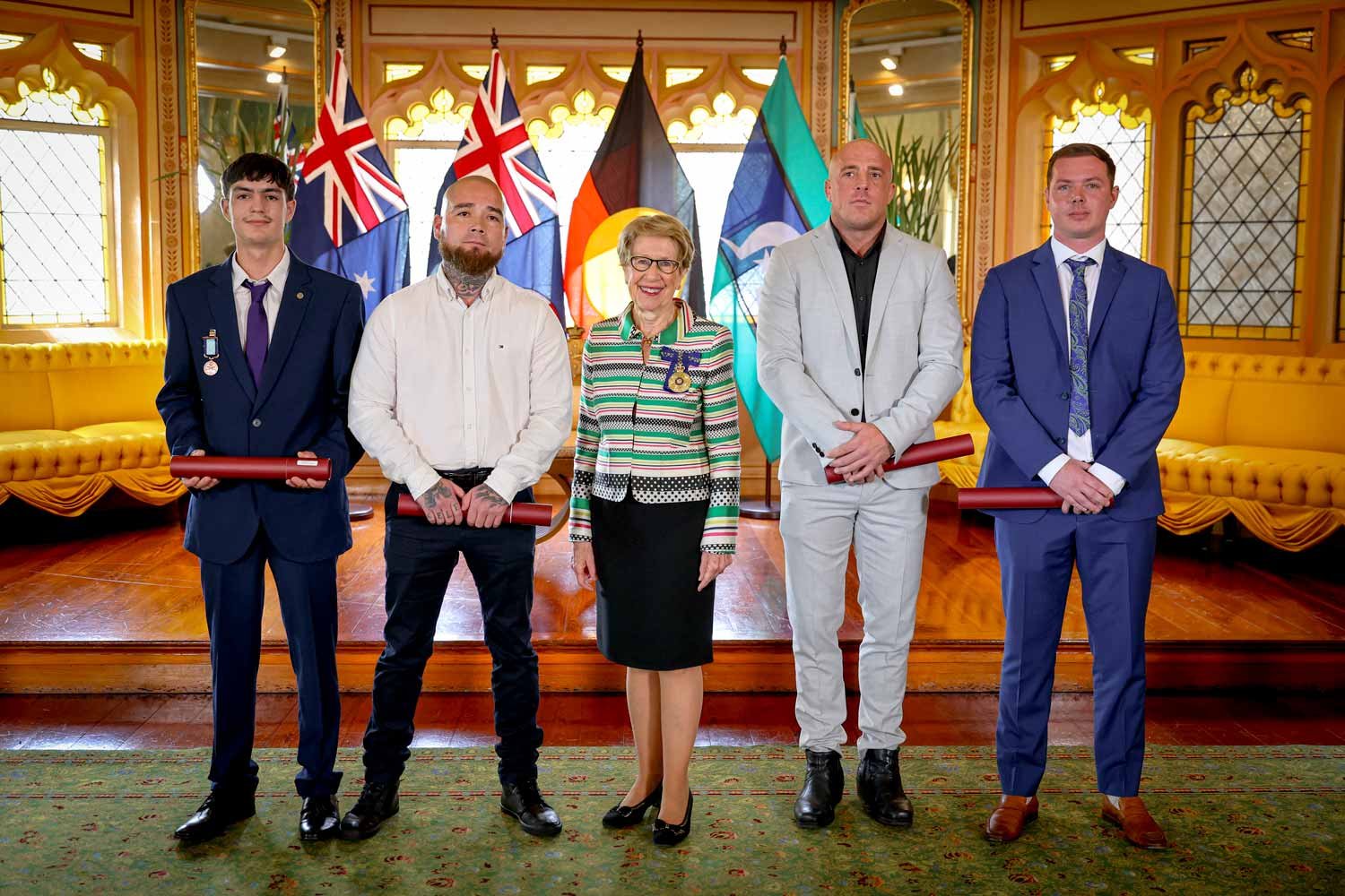 Four men stand with Her Excellency the Governor, all are smiling as they proudly wear their medals.