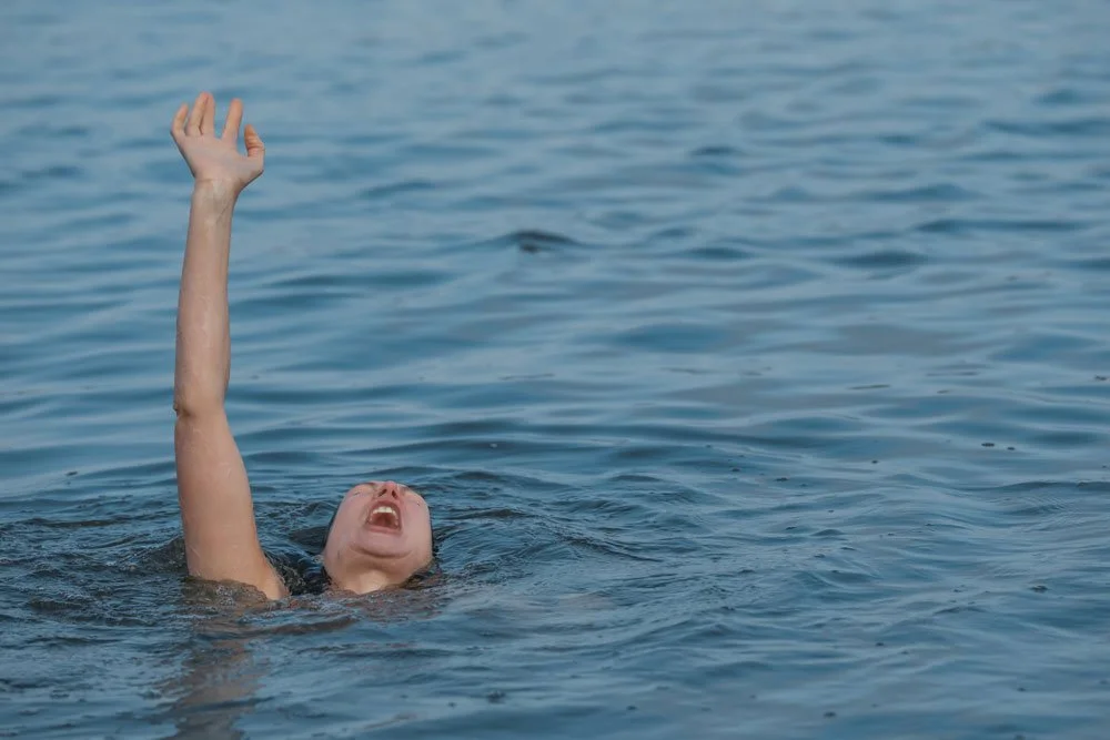 A swimmer in peril. One arm raised in the ocean, waiting for a life saver