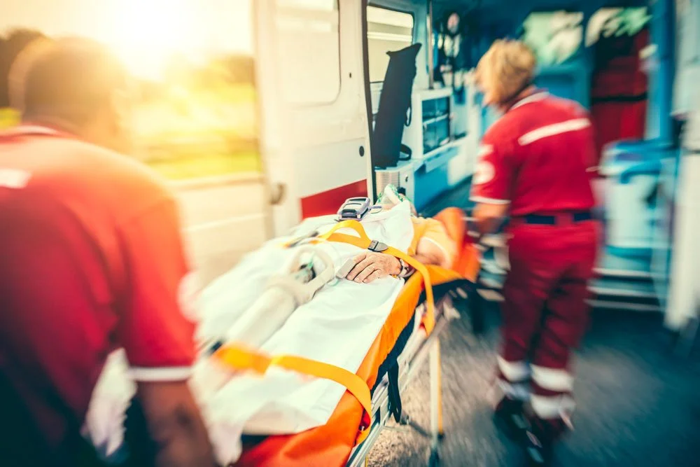 Two paramedics wheel a patient on a gurney into an amulance