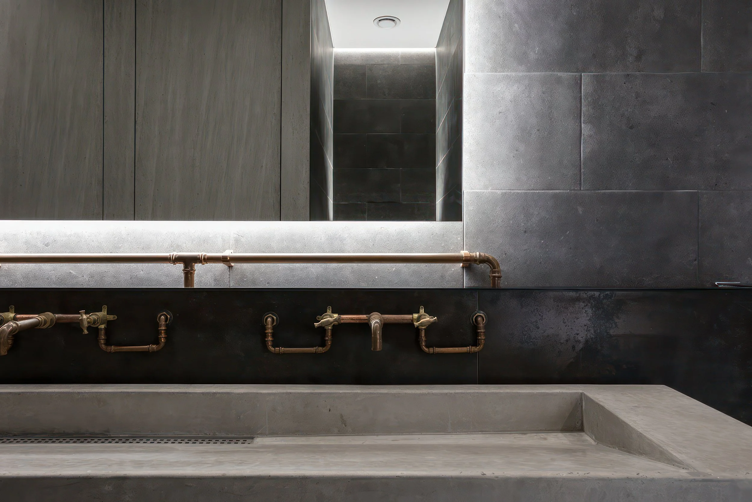 Modern industrial bathroom with concrete sink, copper pipes, and dark stone tiles.