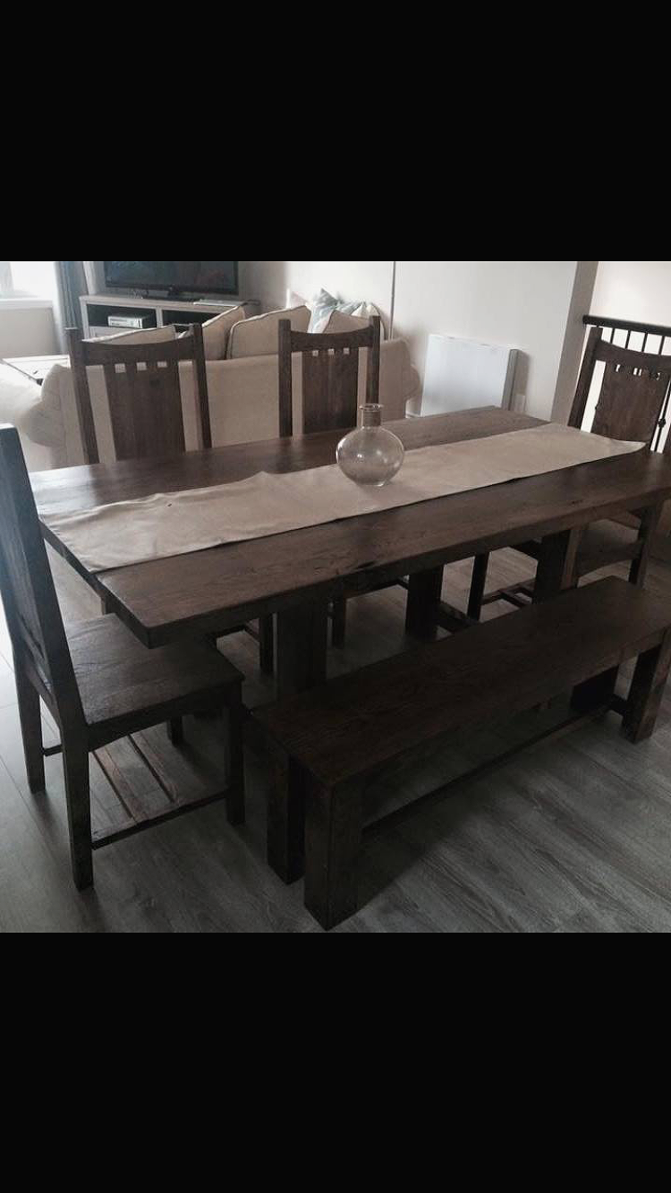 Wooden dining table with chairs and a bench, with a neutral-colored table runner and a glass vase, in a living room setting.