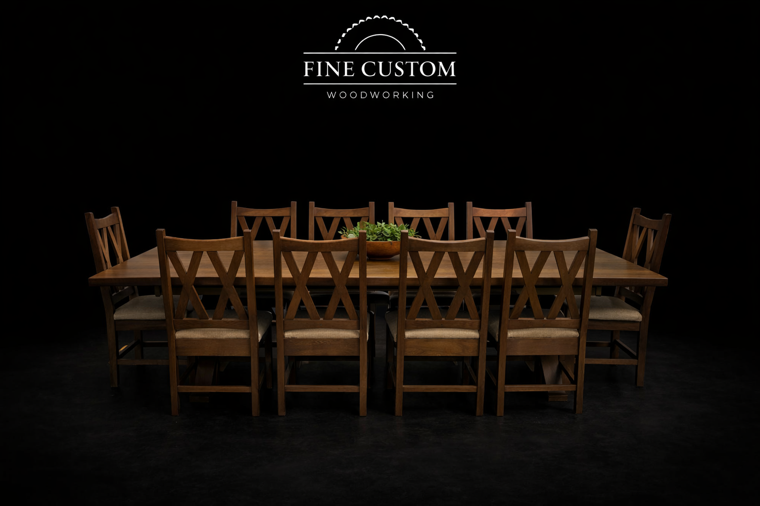 A wooden dining table with nine matching wooden chairs arranged around it, set against a dark background. There is a bowl of greenery on the table and a logo for Fine Custom Woodworking at the top.