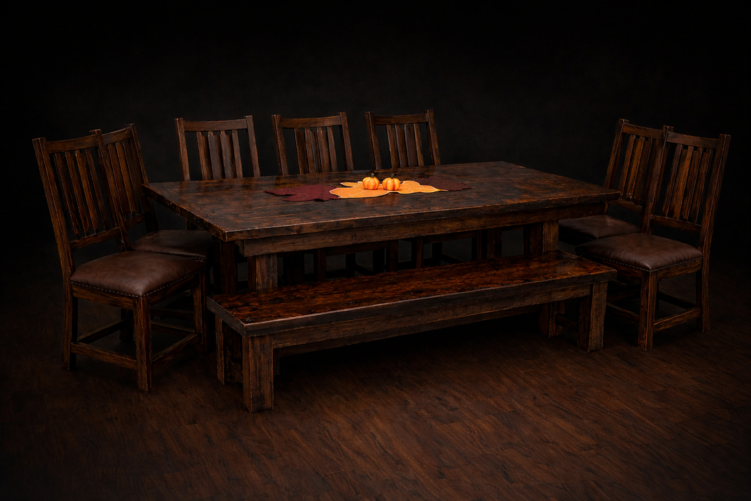 Wooden dining table with six chairs, fall leaves, and two small pumpkins in the center, set against a black background.