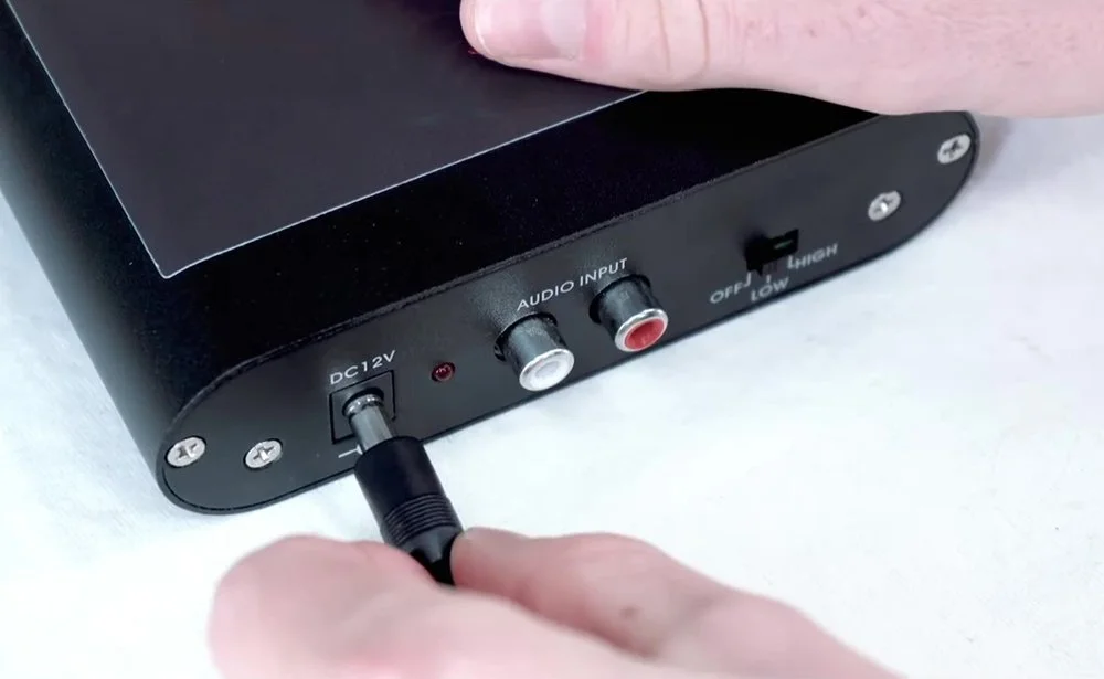 Close-up of a person connecting a power cable to a device with audio input and a switch.