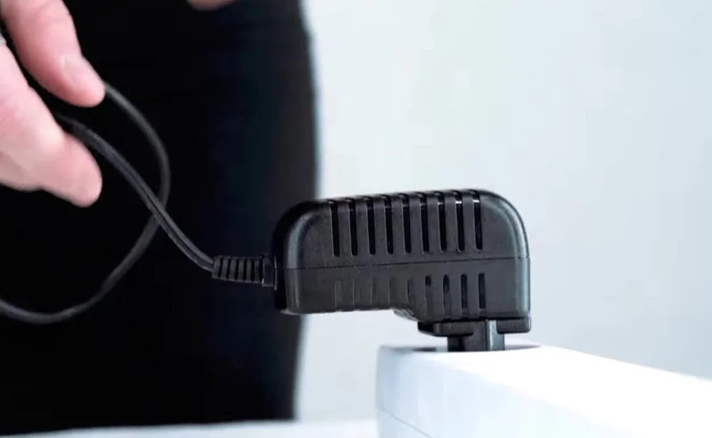 Person plugging a black power adapter into a white power strip