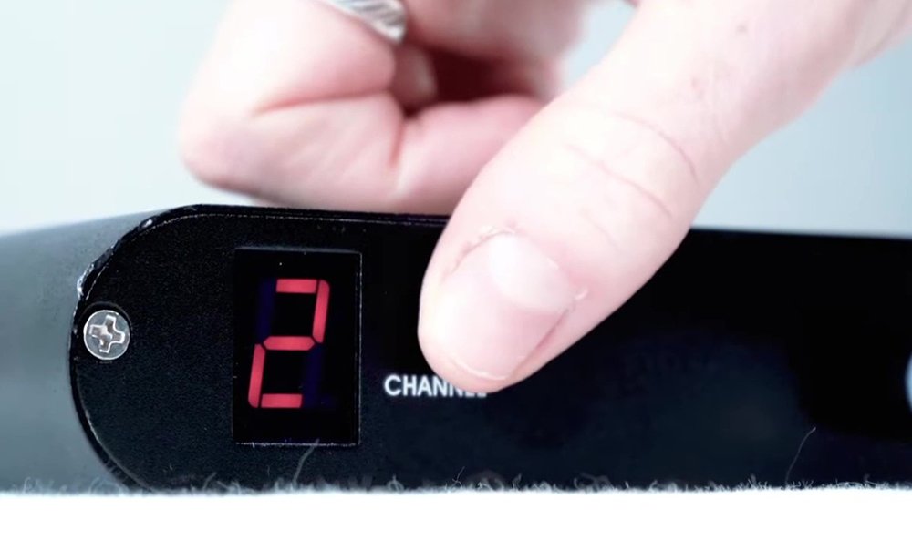 Close-up of a finger adjusting the channel on a device with a digital display showing the number 2.