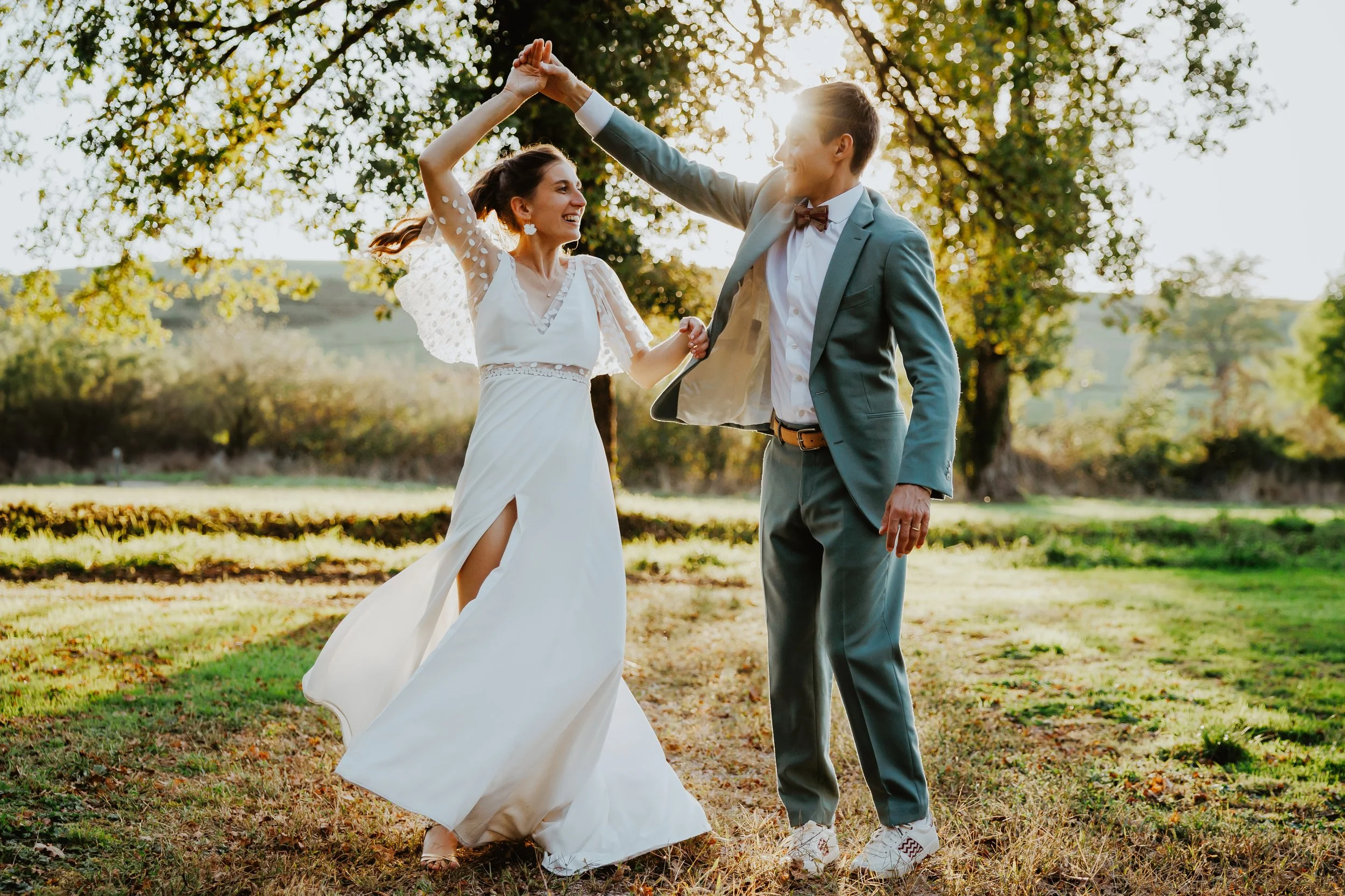 Un couple danse dans un parc en plein air lors d'un mariage ensoleillé, avec des arbres en arrière-plan.