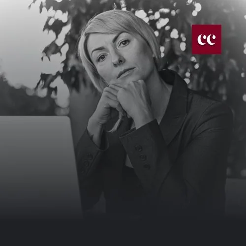 Black-and-white image of a thoughtful professional woman sitting at a desk leadership, resilience, cover image for Rezan Manan’s article ‘Midlife, Menopause In The Boardroom: Leading Through Your Strongest, Most Challenging Years’ on rezanmanan.com